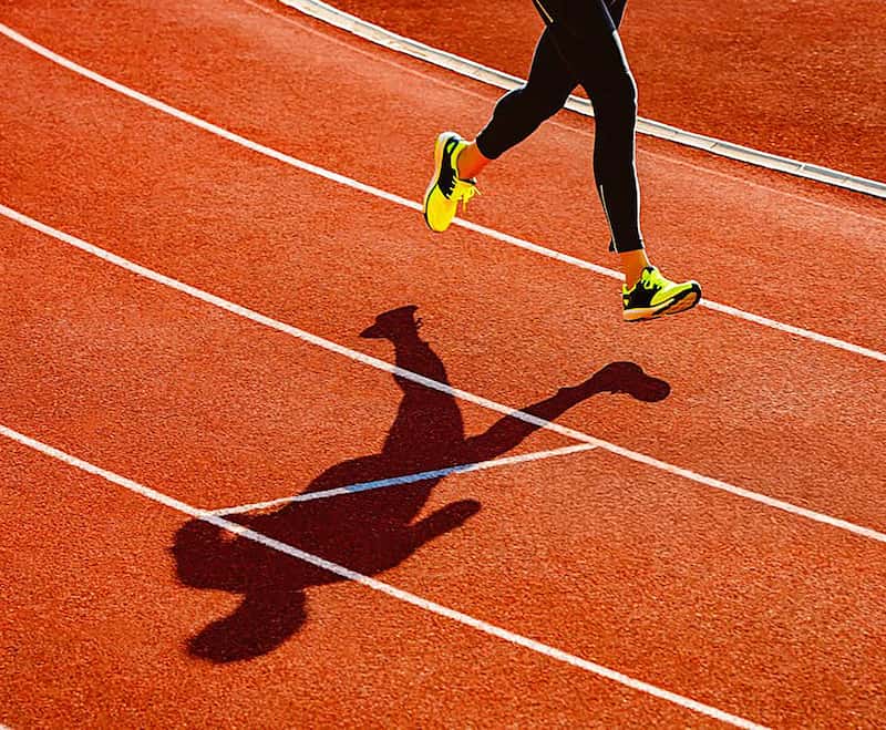 Runner in yellow shoes striding across a red running track